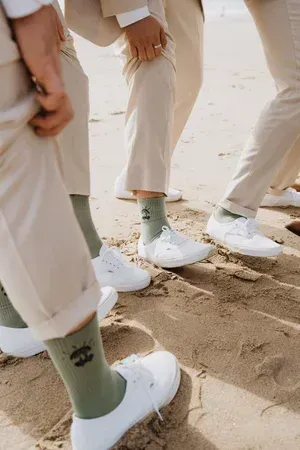 People in beige pants and white sneakers standing together on sandy ground.