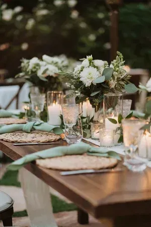 Elegant outdoor dining table with white floral centerpieces, candles, and green napkins