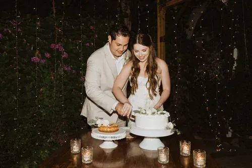 Couple cutting a white wedding cake on a candlelit table in a dark garden setting