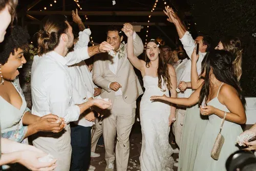 Guests dancing and cheering at a lively indoor wedding reception, with the bride and groom in the center