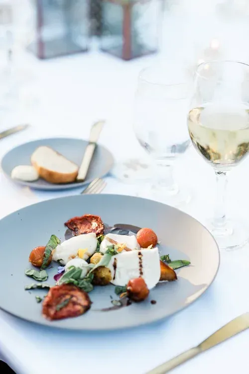 Plated gourmet dish with bread and a glass of white wine on a bright restaurant table