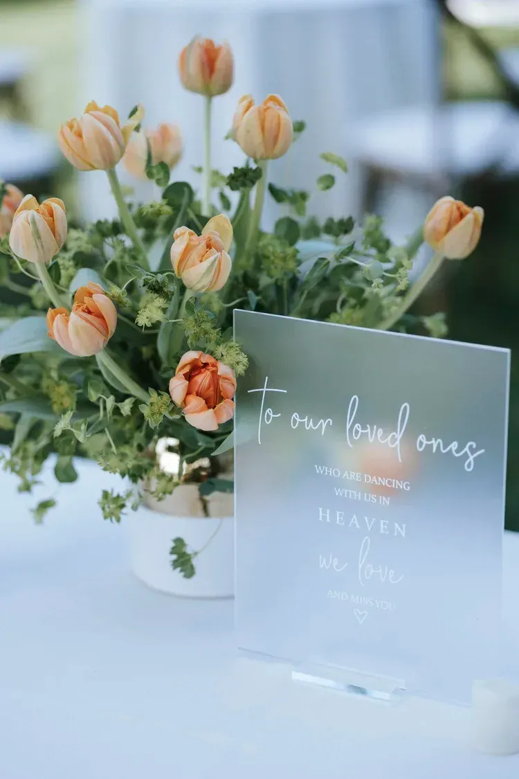 Peach tulips in a white pot beside a clear acrylic sign on a table