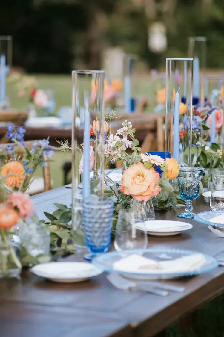 Outdoor table set with blue glassware, white plates, and floral centerpieces for an elegant event