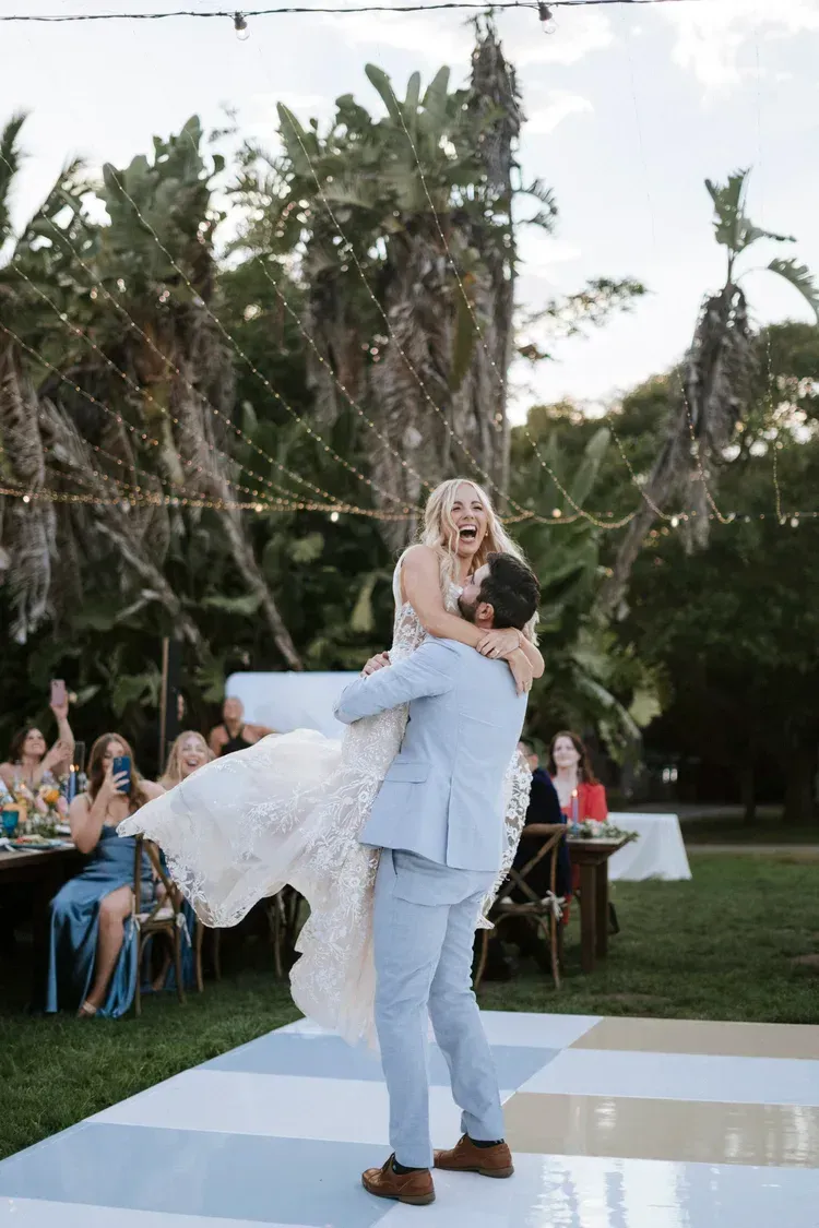 Man in light blue suit lifting a smiling bride in a white dress on a wedding dance floor outdoors