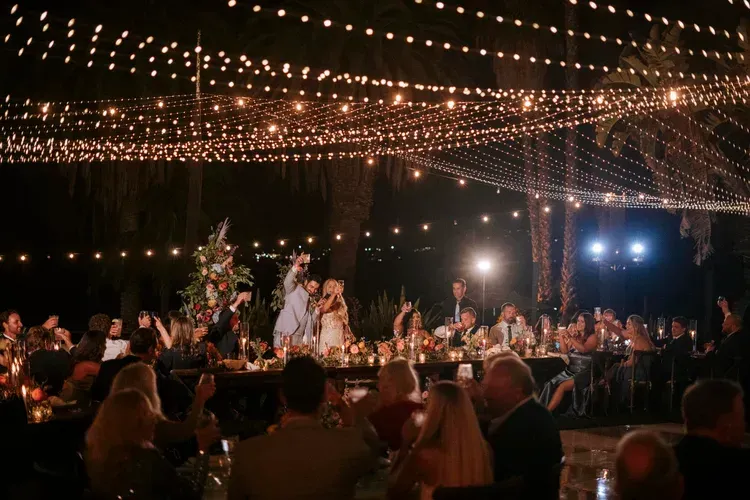 Elegant outdoor dinner reception under string lights with guests seated at long tables at night