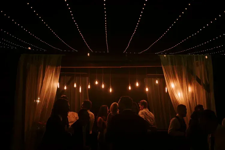 Dimly lit stage with hanging bulbs, curtains, and silhouetted people gathered in front