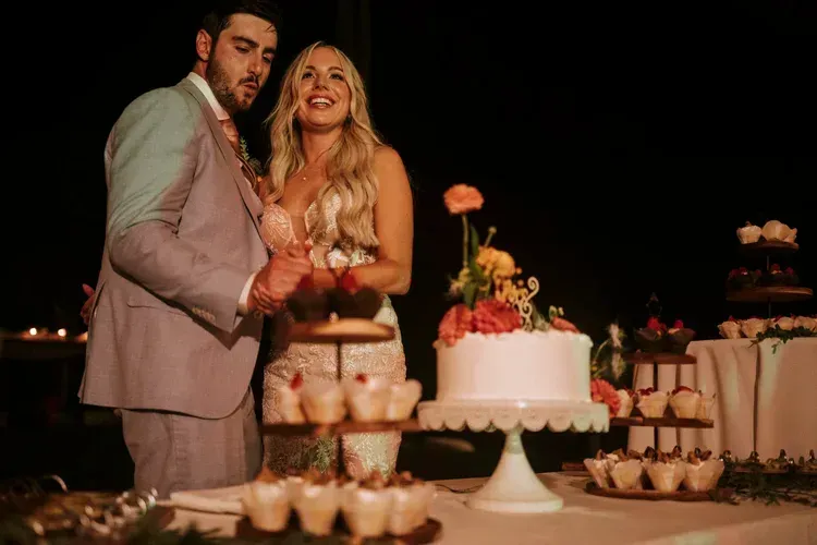 Couple posing by a decorated cake table at a candlelit celebration with cupcakes and flowers