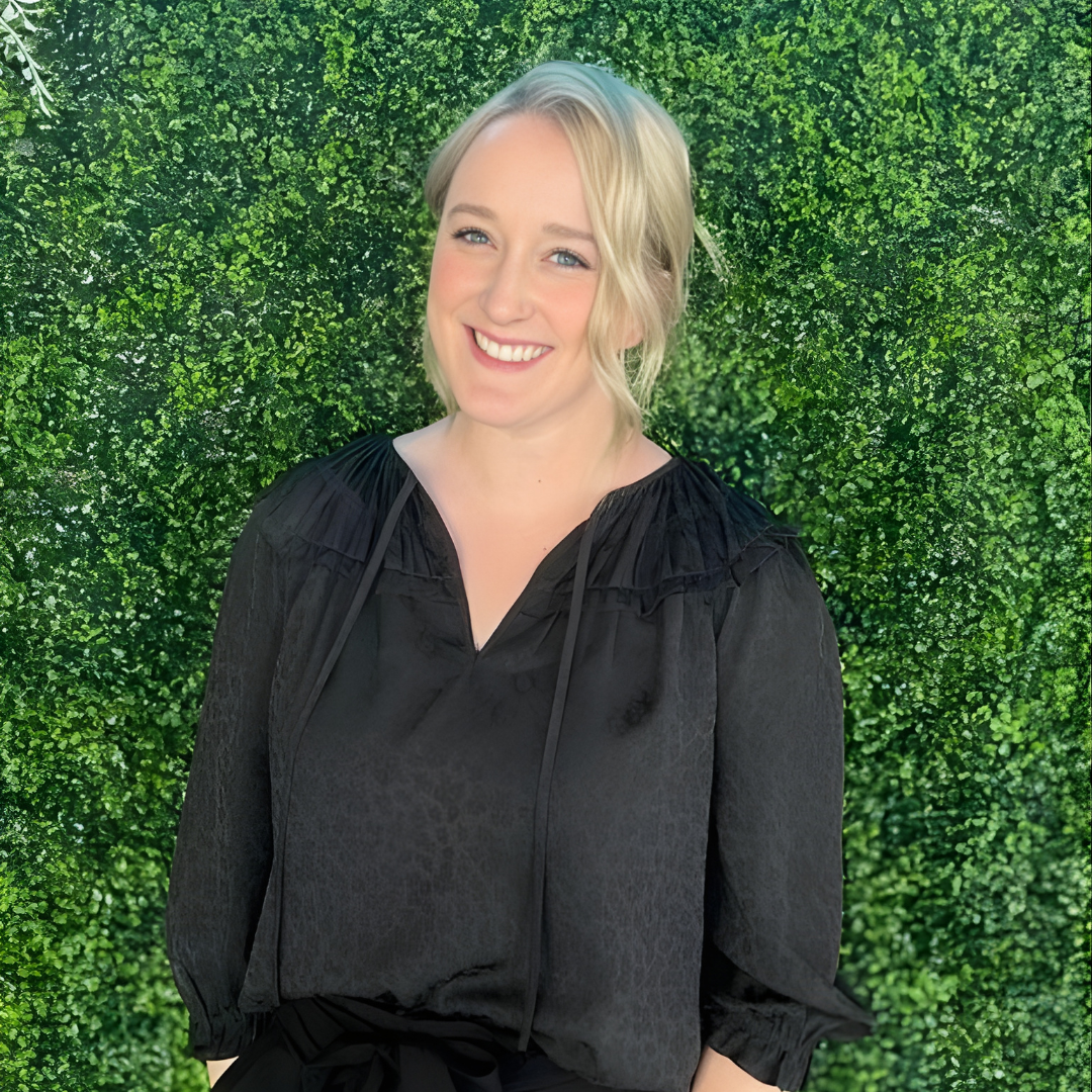Smiling woman in a black blouse standing in front of a green hedge wall