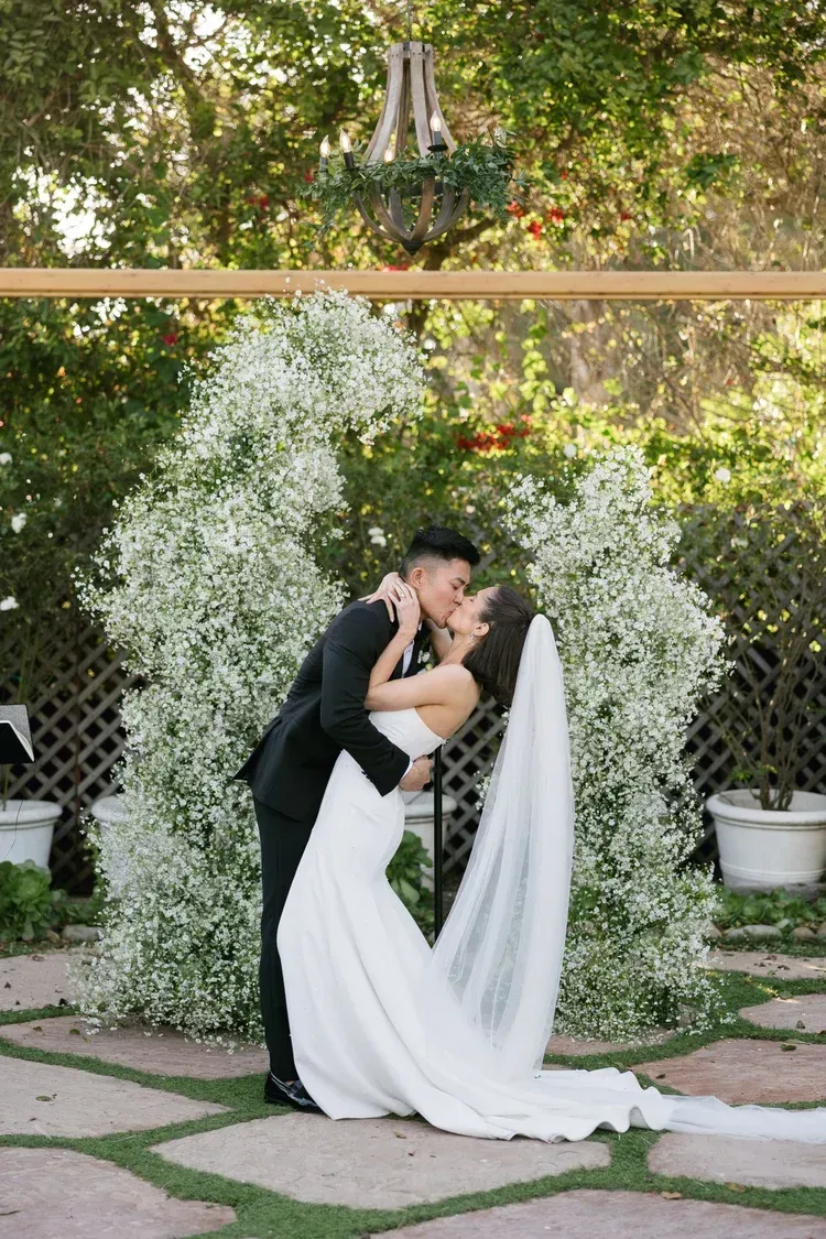 Wedding couple kissing beneath a floral arch in a garden ceremony