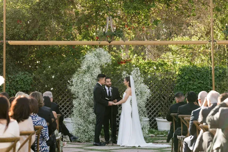 Bride and groom exchanging vows under a wooden arch at an outdoor wedding ceremony