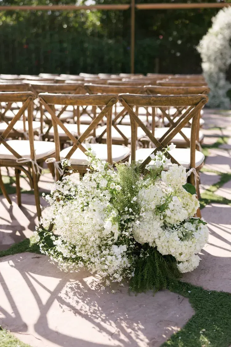 White floral arrangement beside wooden chairs at an outdoor event