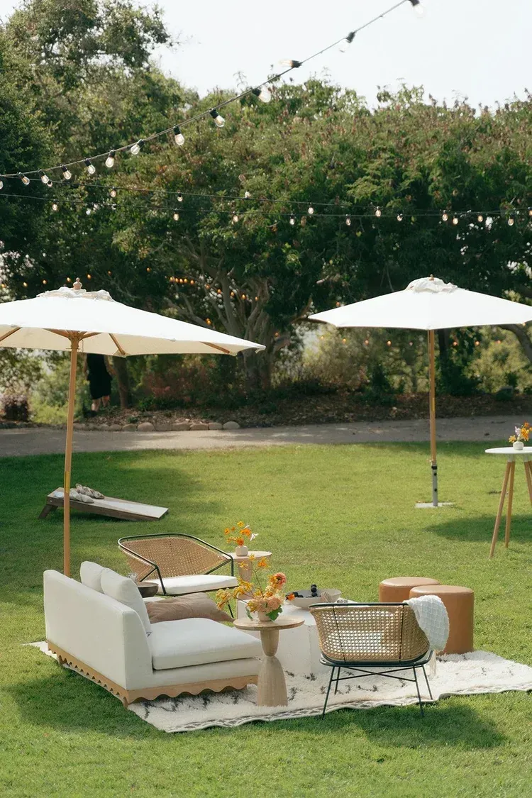 Outdoor patio with white sofa, wicker chairs, umbrellas, and a grassy yard with trees in the background