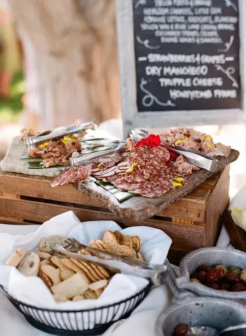Charcuterie spread with sliced meats, crackers, and cheese on rustic wooden crates at an outdoor table