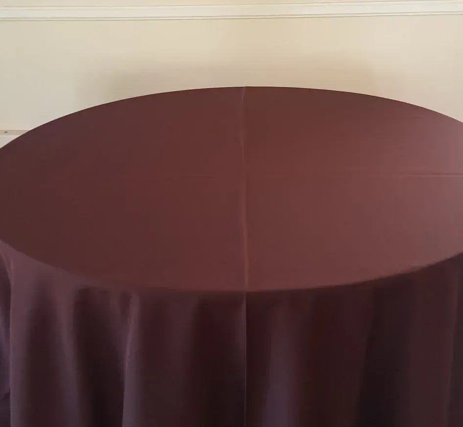Round table covered with a dark burgundy tablecloth against a beige wall.