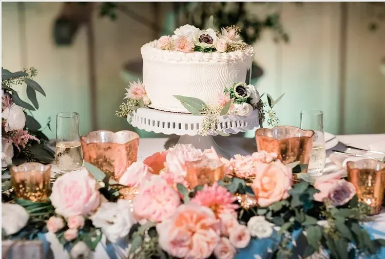 Elegant white floral cake on a decorated table with pink flowers and copper accents