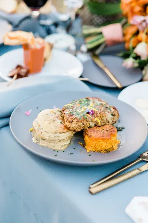 Plated gourmet dish on a blue table setting with flowers and gold utensils
