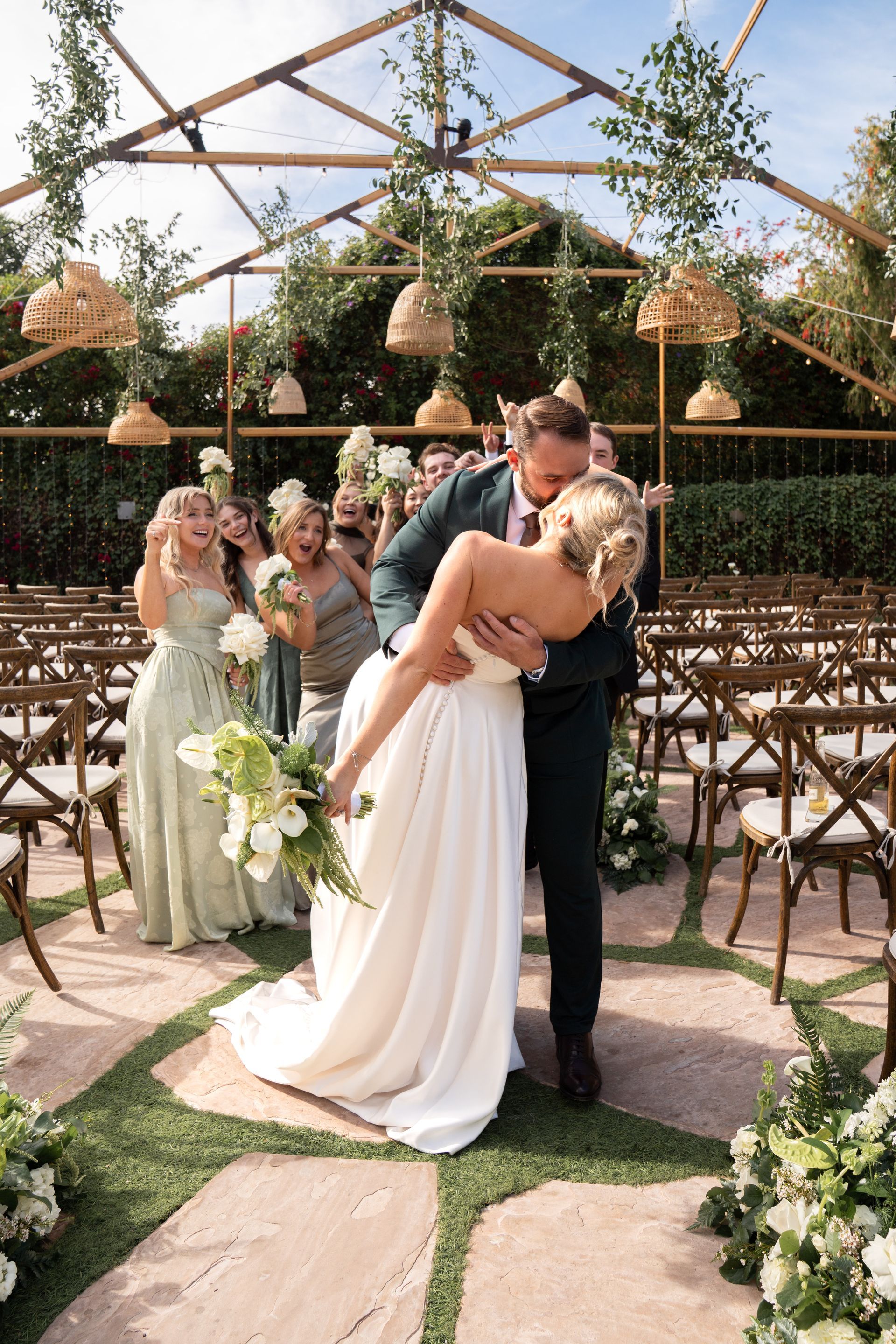 Bride and groom kissing in a garden wedding arch with bridesmaids nearby
