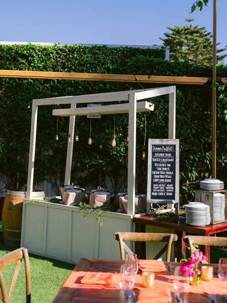 Outdoor coffee cart with green front, chalkboard menu, and cups under a wooden canopy on a lawn
