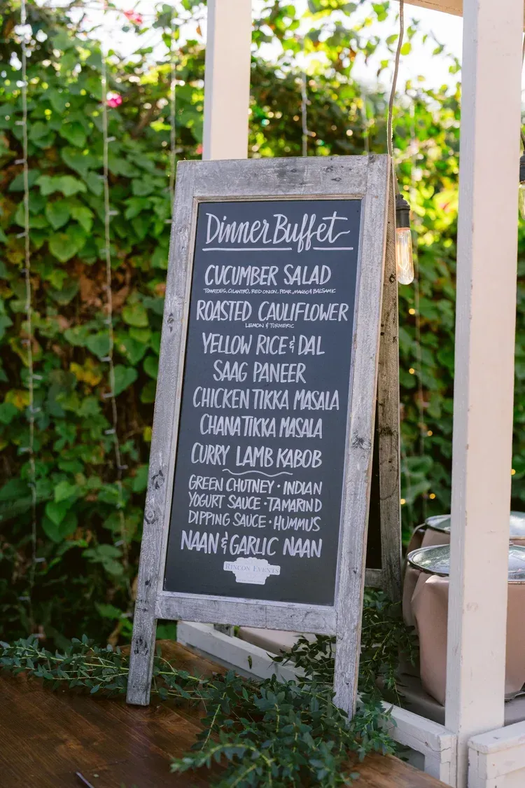Outdoor chalkboard café menu on a patio, framed by white posts and greenery.
