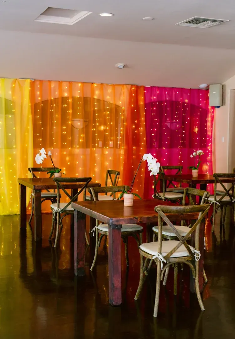 Decorated banquet room with orange and magenta drapes, string lights, and tables and chairs set up