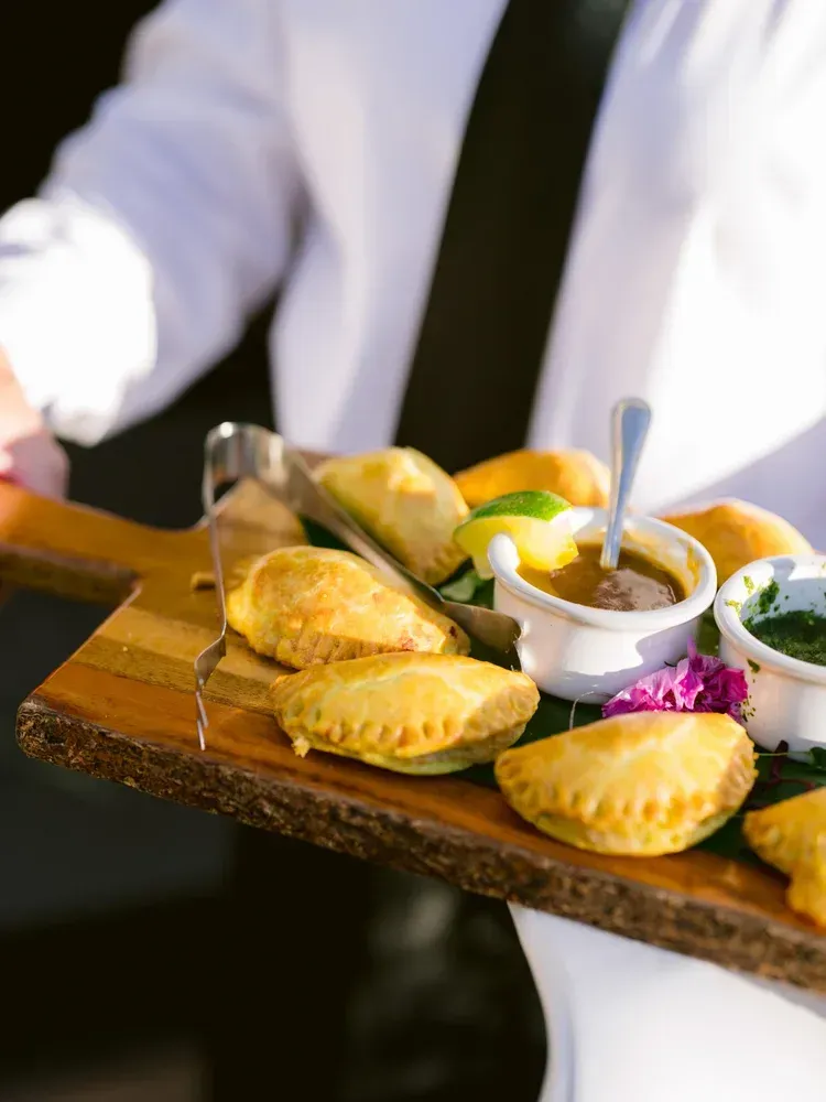 Server carrying a wooden tray with empanadas, sauces, and lime wedges at a restaurant