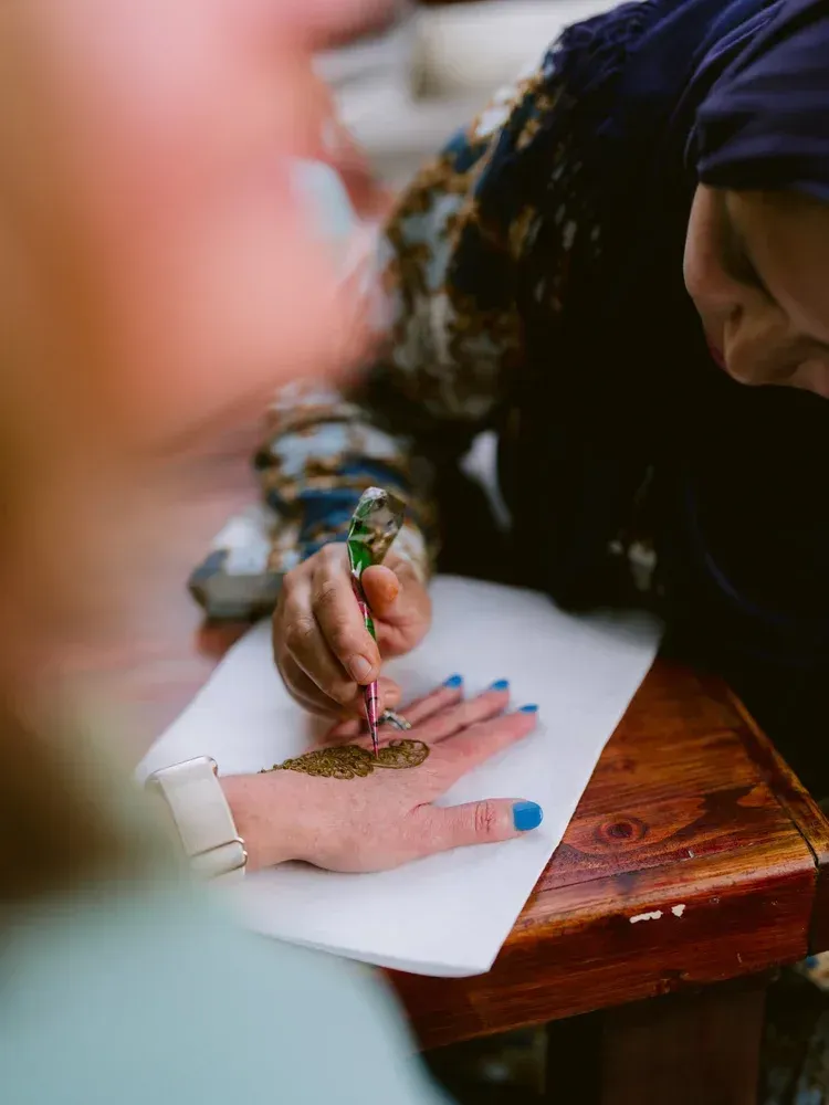 A henna artist decorating a hand with intricate designs on a white paper-covered table