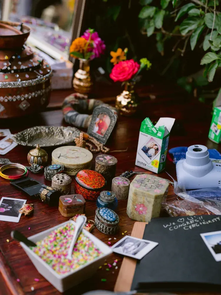 Assorted colorful handmade craft items and trinkets arranged on a table with flowers and small containers