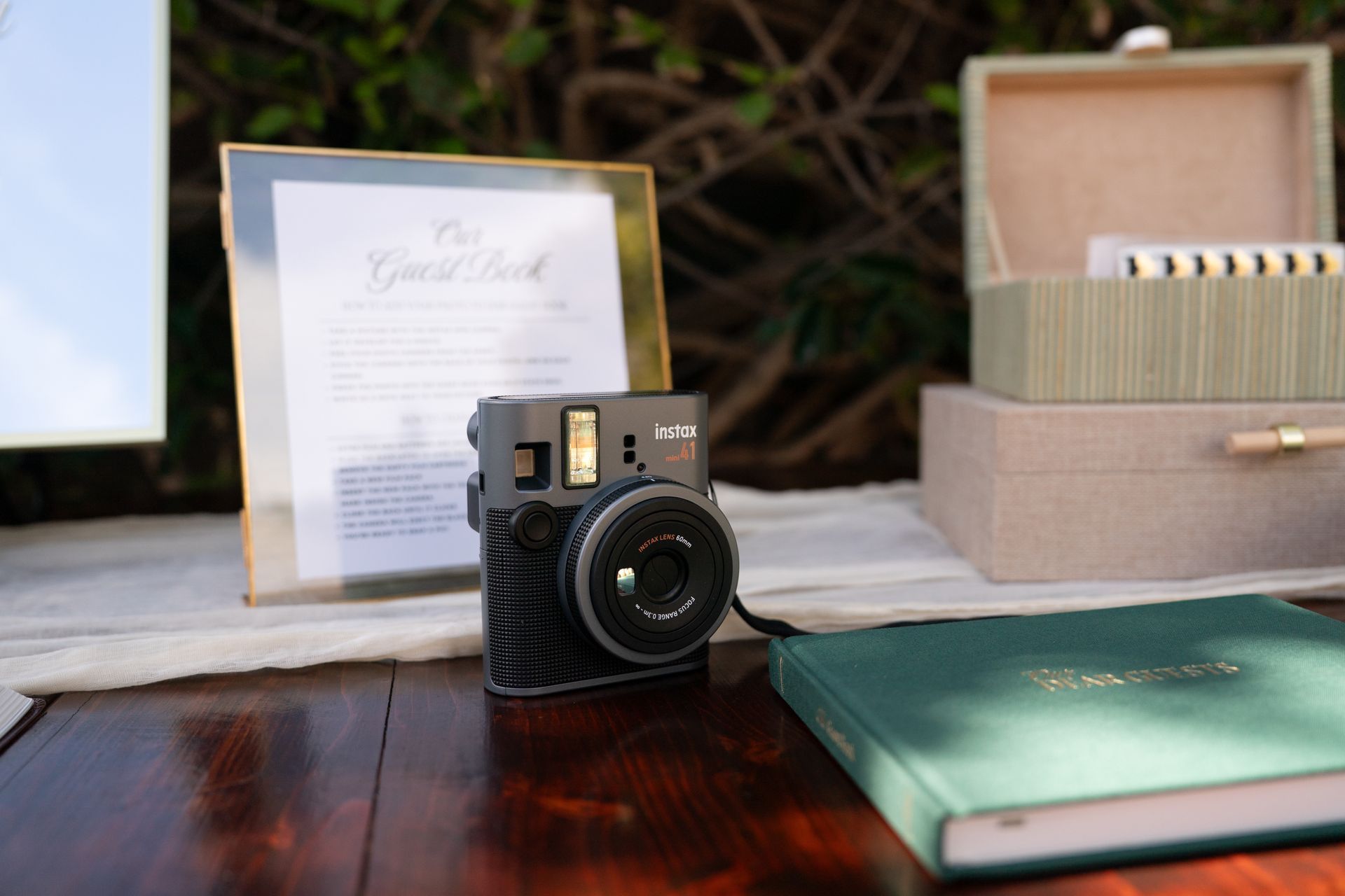 Compact vintage-style camera on a wooden table with a green notebook and open gift box in the background