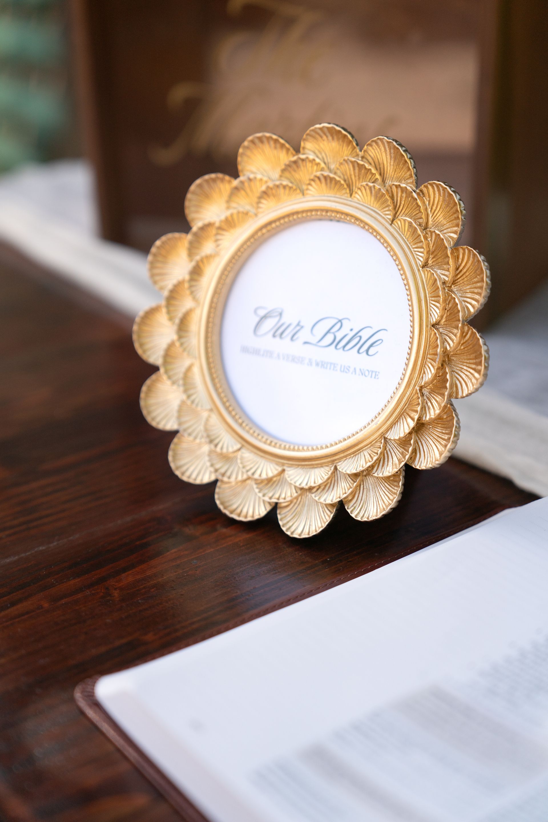 Gold oval frame on dark wood table, displaying “Cat Bible” with a blurred open book in the foreground
