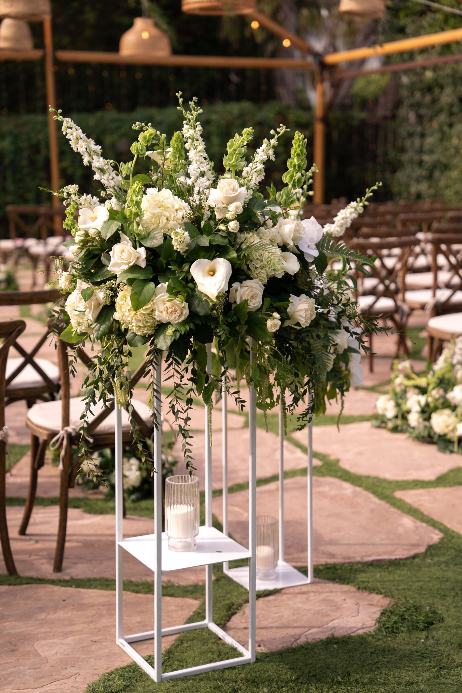 White floral arrangement on a tall geometric stand at an outdoor wedding venue