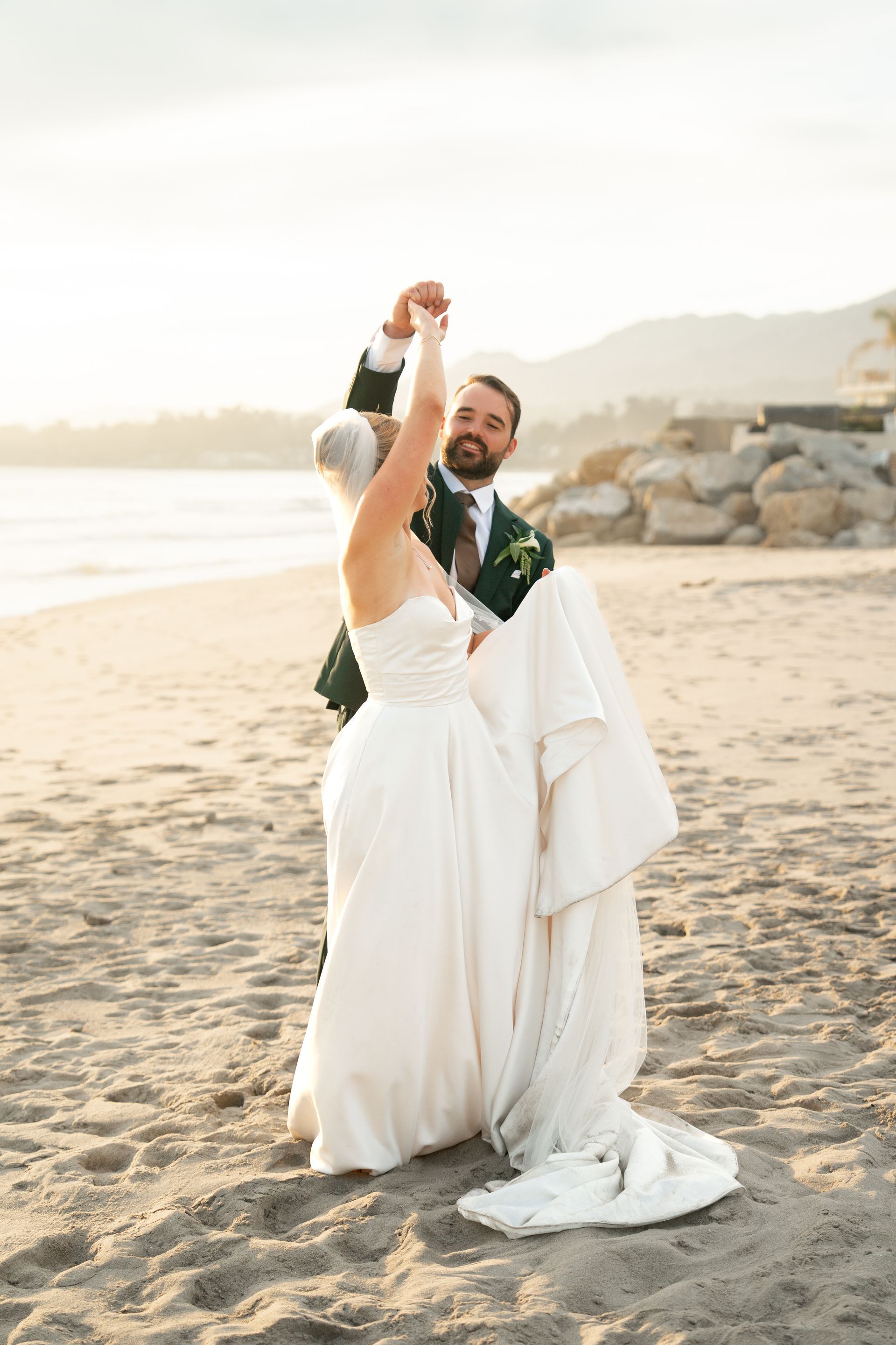 Couple in wedding attire dancing on a sandy beach at sunset