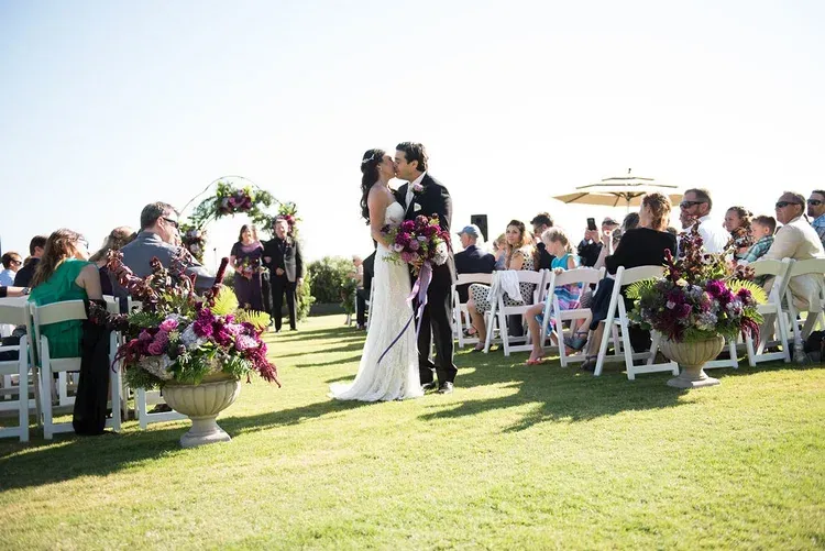 Outdoor wedding ceremony on a lawn, with a couple embracing at the altar and guests seated nearby.