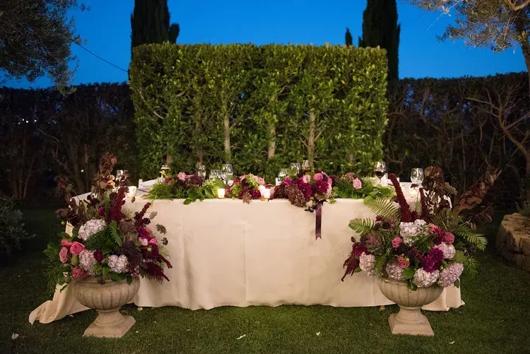White draped table with pink and white floral arrangements in a nighttime garden setting