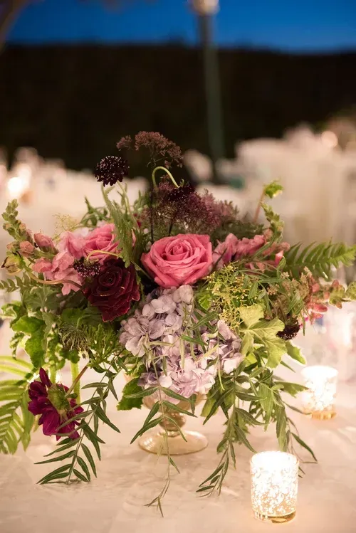 Pink and purple floral centerpiece with greenery on a softly lit table