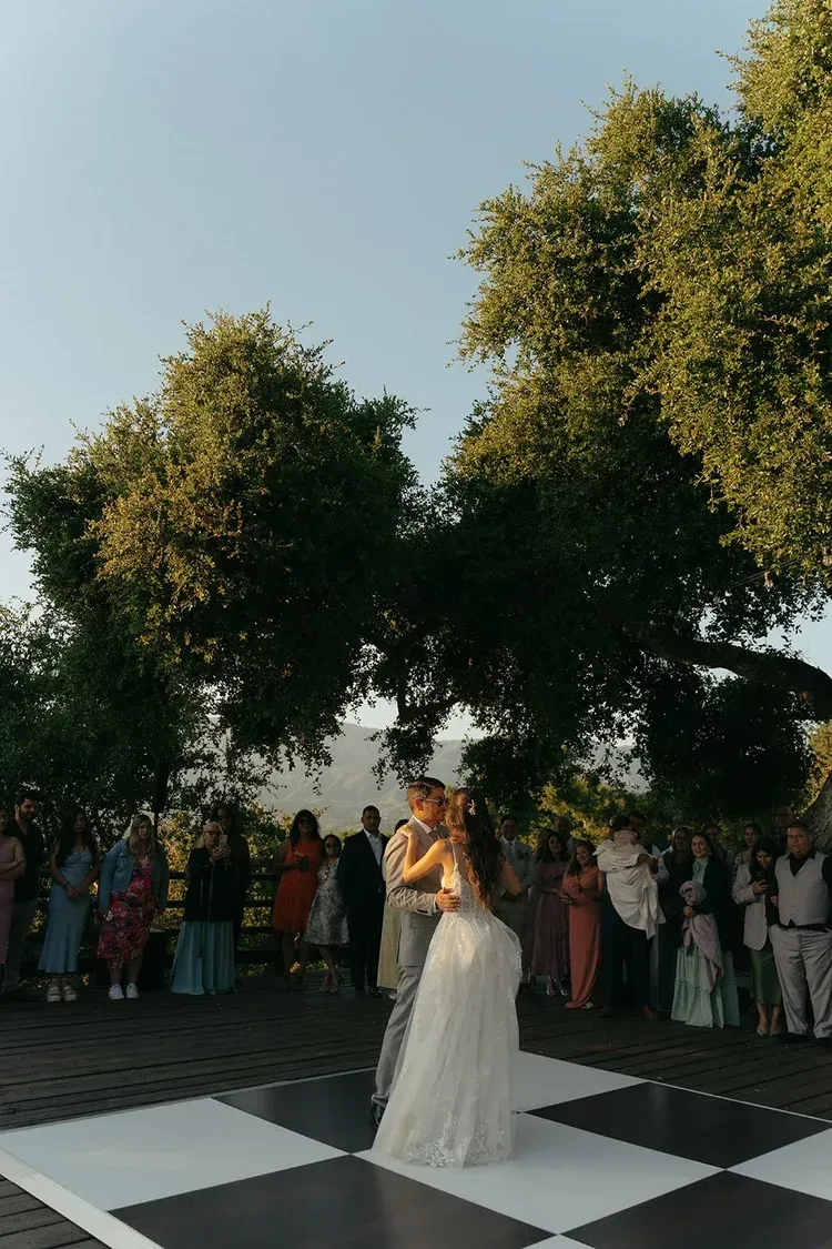 Couple dancing on a black-and-white checkered floor at an outdoor wedding reception