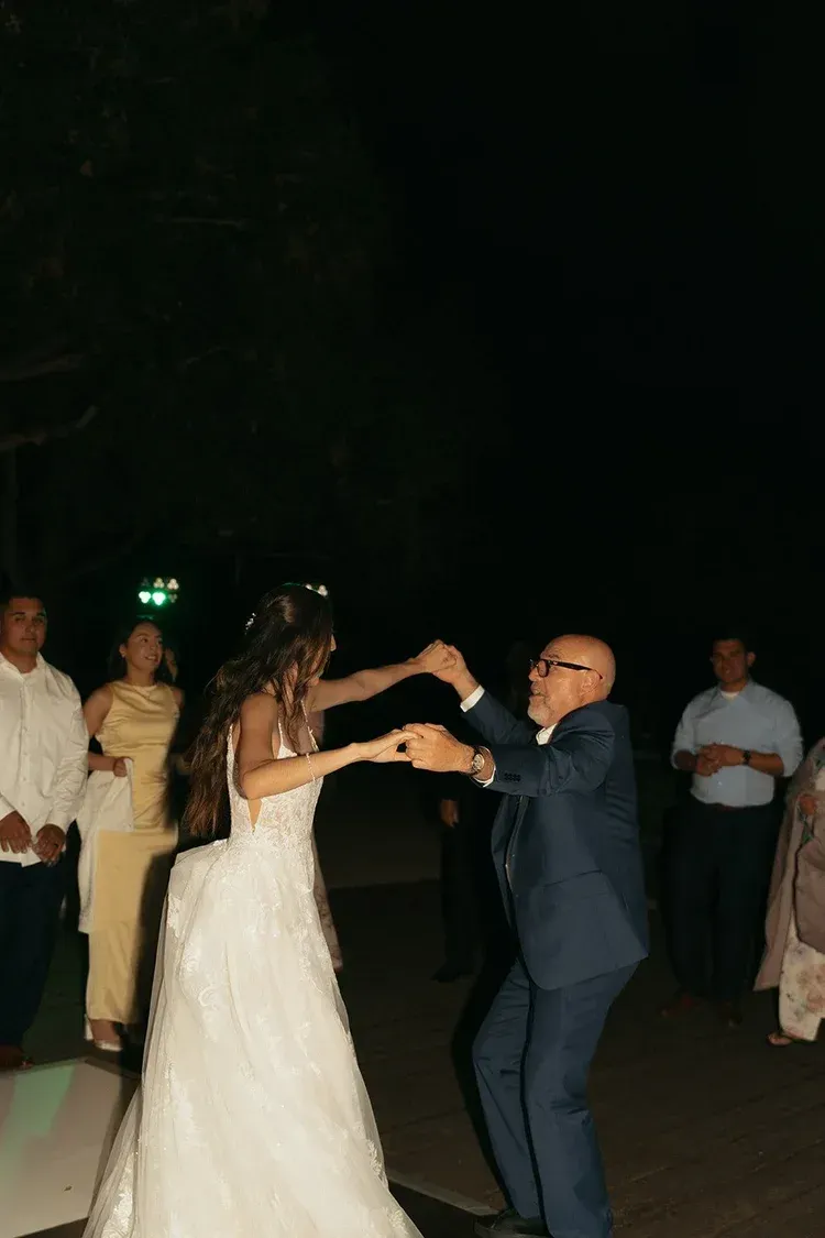 Bride in a white gown dancing with a man in a dark suit at an outdoor nighttime celebration