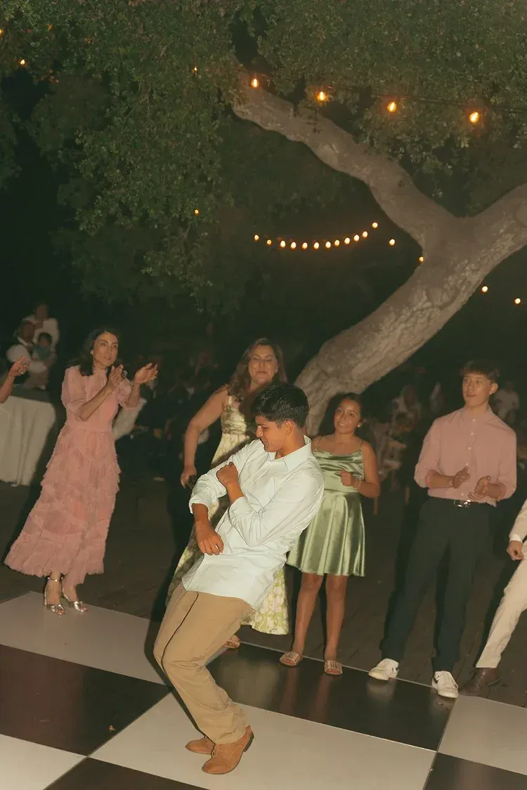 Person dancing on a black-and-white checkered floor at an outdoor evening party with string lights.