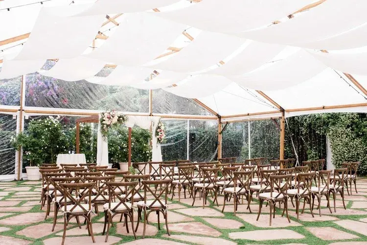 Outdoor event tent with rows of wooden chairs on a patterned stone floor, under a white canopy