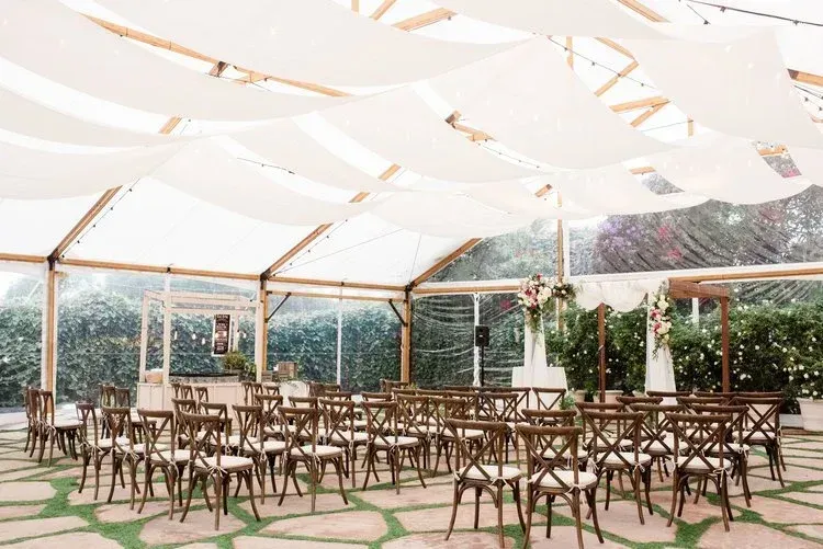 Empty outdoor event tent with rows of wooden chairs under a white canopy