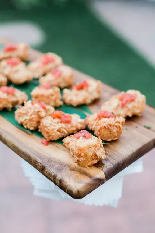 Breaded appetizer bites topped with pink garnish on a wooden serving board