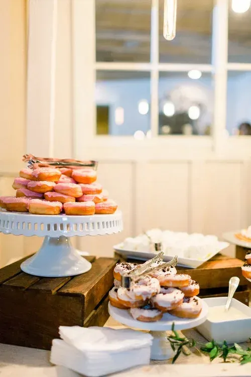 Dessert table with donuts and pastries on stands in a bright room near a window