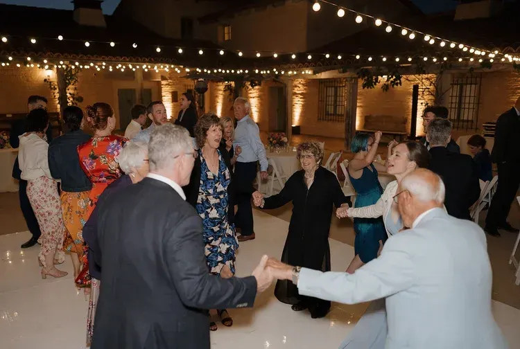 People dancing at a warmly lit evening reception with string lights and a brick courtyard backdrop