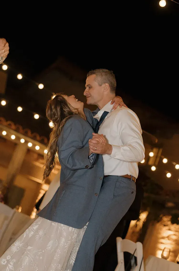 Couple dancing at a nighttime reception under warm string lights