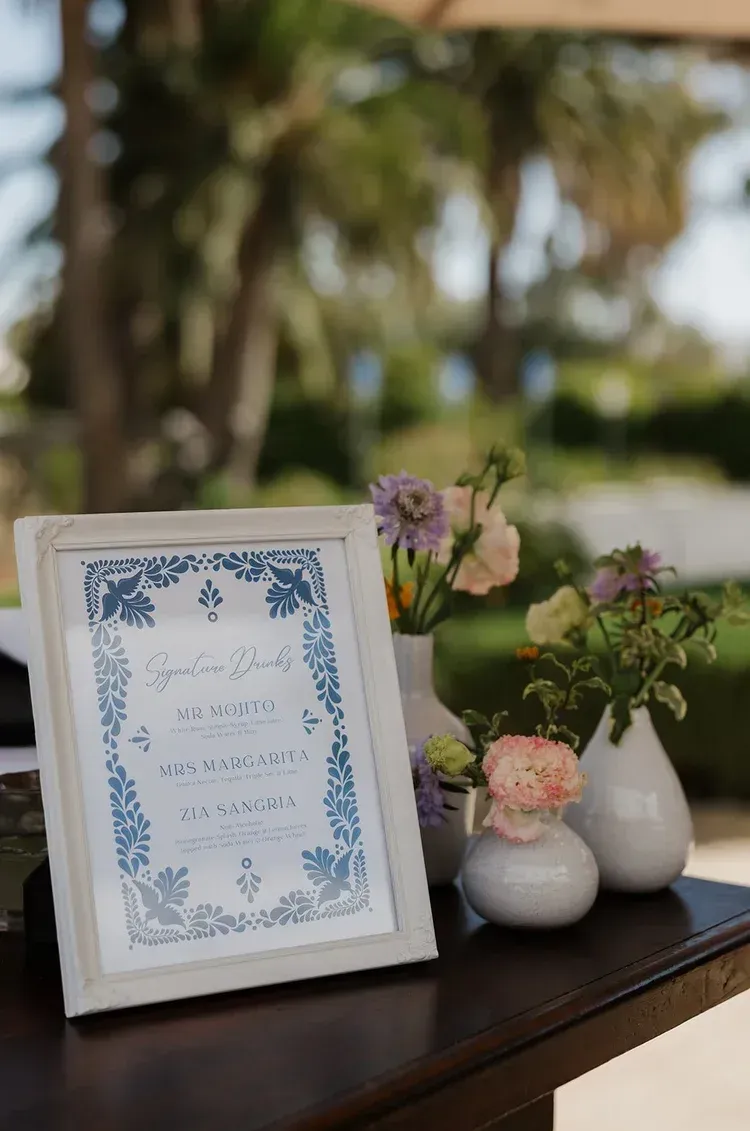 Framed floral sign beside small white vases with flowers on a table outdoors