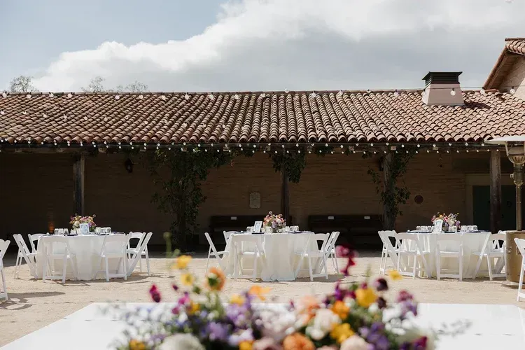 Outdoor banquet tables under a tiled patio with flowers in the foreground