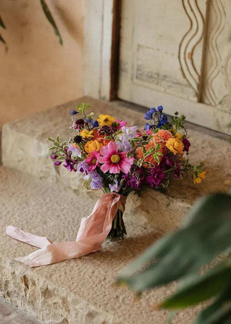 Bouquet of colorful wildflowers on a stone floor, with a pale pink ribbon beside it.