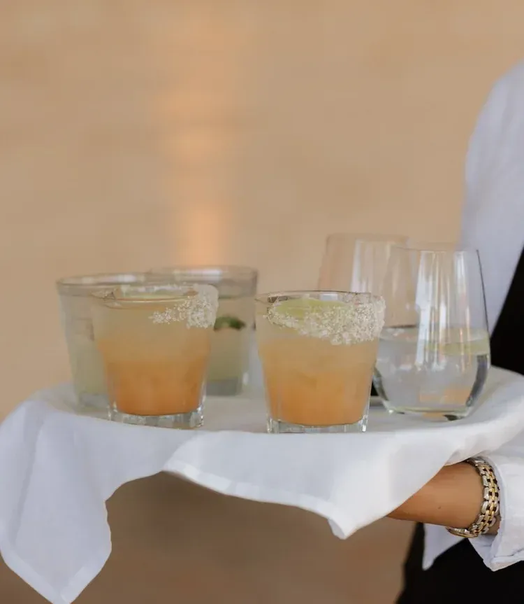 Three orange drinks and an empty glass on a white-clothed tray held by a server
