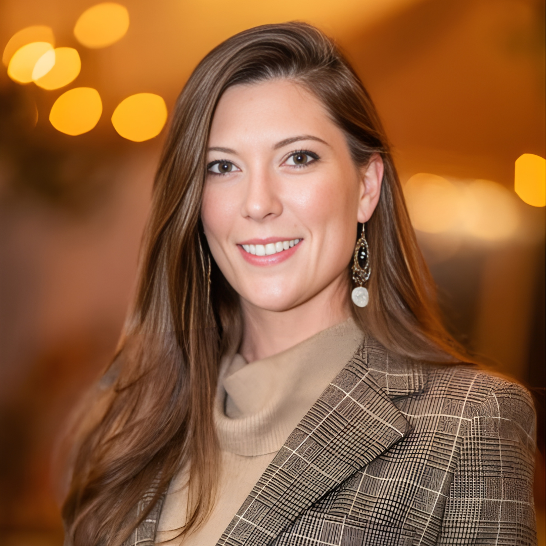 Smiling woman in a plaid blazer against a warm, blurred background
