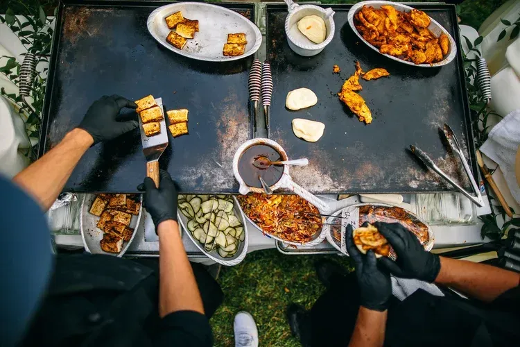 People grilling and serving food around a round outdoor barbecue table