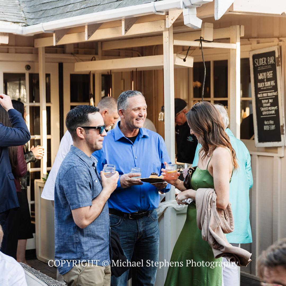 People chatting with drinks outside a wooden storefront in daylight